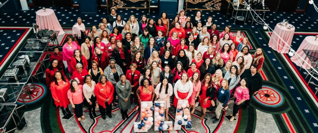 Almost 100 women smiling at the camera wearing red