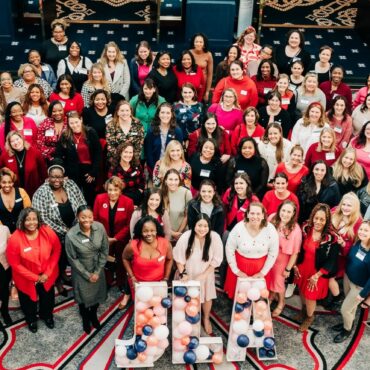 Almost 100 women smiling at the camera wearing red