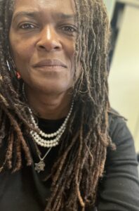 Woman with long light brown locks wearing a black shirt and pearl necklaces